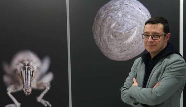 El artista Leo Tena posa con una de las fotos que expone en la galería Ármaga. Foto: CUEVAS / Diario de León.